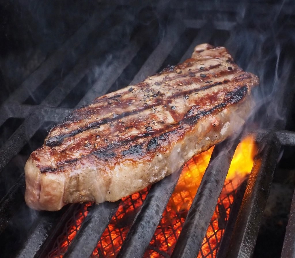 Thick steak searing over hot coals on a grill