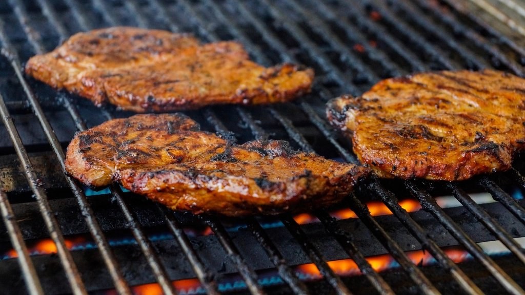 Chicken pieces cooking over open flame on a grill